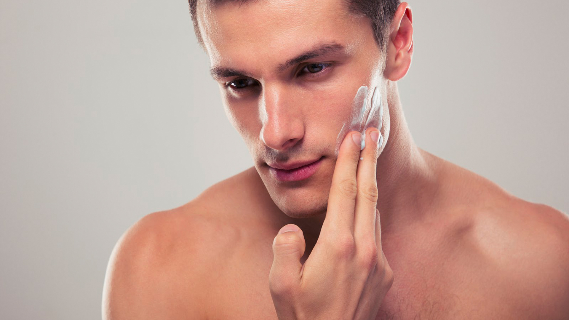 Imagem com um homem passando um creme facial em seu rosto durante o skincare.