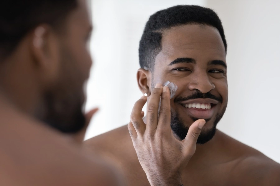 Homem sorrindo ao fazer sua rotina de skincare.