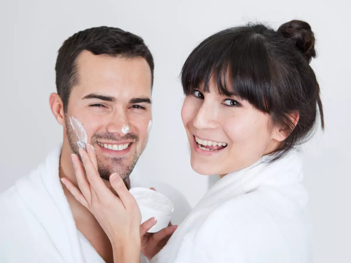 Imagem mostra uma mulher aplicando creme facial no rosto de um homem.