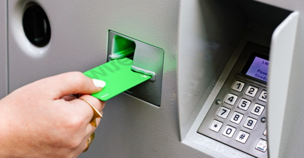 Mão de uma pessoa inserindo um cartão verde da Wise em um terminal de pagamento.
